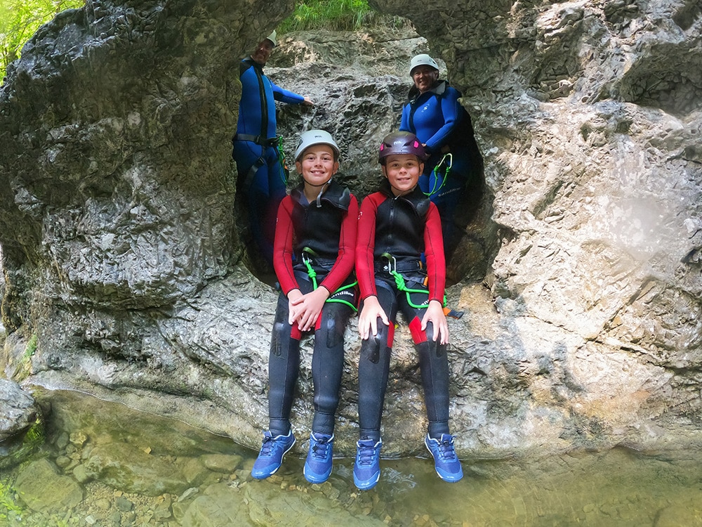Family enjoying a canyoning adventure in Salzburg's Almbachklamm gorge, wearing wetsuits and safety equipment. Canyoning with kids is the perfect activity in Salzburg for the whole family.