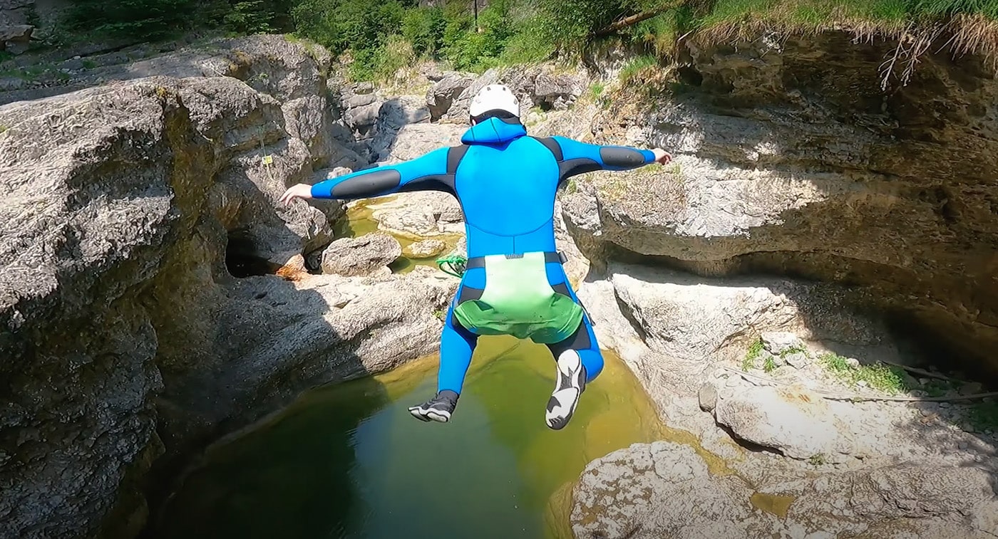 Man jumping into a water pool in the Almbachklamm canyon, showcasing exciting activities like climbing, swimming, and waterfall slides in Salzburg.