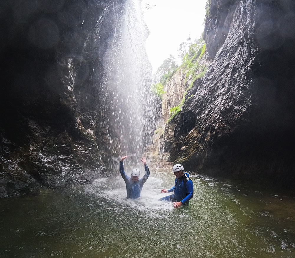 Strubklamm Canyoning - waterfall experience in Salzburg Strubklamm Canyoning Austria - Two young men enjoy a natural waterfall shower under the up to 200 m high rock walls of the Strubklamm (Faistenau / Ebenau / Wiestal) on a guided canyoning tour in Salzburg, Austria.