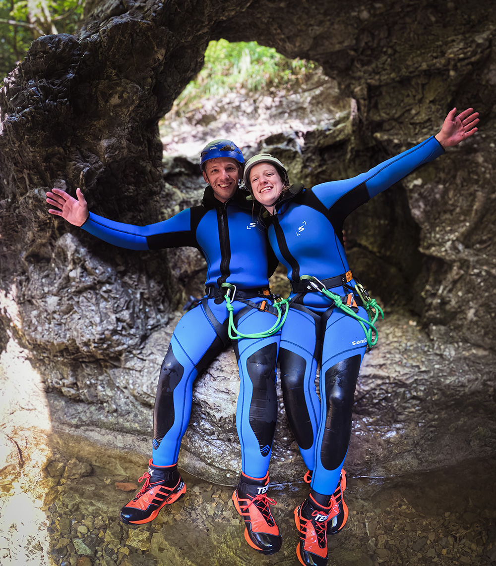 Zwei Personen im Neoprenanzug sitzen Arm in Arm in einer Felsformation bei einer Canyoning Tour in Salzburg in der Almbachklamm bei Hallein - ideales Erlebnisgeschenk und Abenteuer Gutschein für Paare, Lieblingsmenschen und beste Freunde.