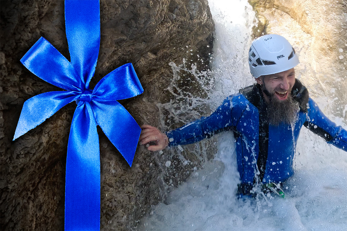 Person in Neoprenanzug und Helm steht mitten in einem Wasserfall in einer Schlucht bei Salzburg - Canyoning Erlebnis als Gutschein für Abenteuer, Junggesellenabschied, Geburtstage, Männergeschenke und Familien.